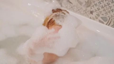 Adorable smiling blonde three years old girl taking bath with white foam bubbles Stock Footage 246714312