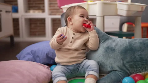 Adorable toddler bitting plastic construction blocks sitting on floor at ki.. Stock Footage 230030695