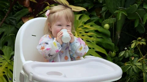 Adorable toddler smiling while learning to drink from an open cup in a high Stock Footage 310619816