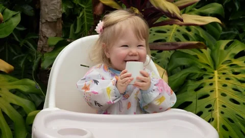 Adorable toddler smiling while learning to drink from an open cup in a high Stock Footage 310619868