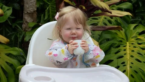 Adorable toddler smiling while learning to drink from an open cup in a high Stock Footage 311654203