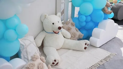 Adorable white teddy bear seated among blue balloons and pillows, creating a Stock-Footage 319247406