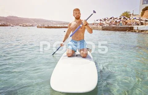 Adult bearded man beginner surfer kneel on paddleboard Stock Photos