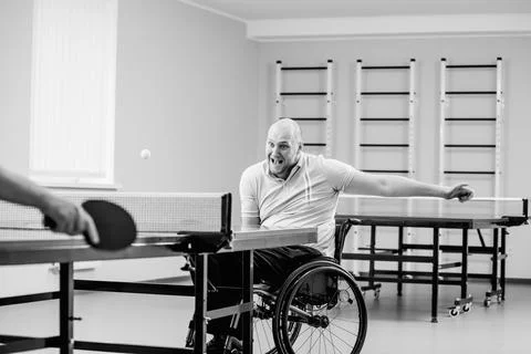 Adult disabled man in a wheelchair play at table tennis with his coach Stock Photos