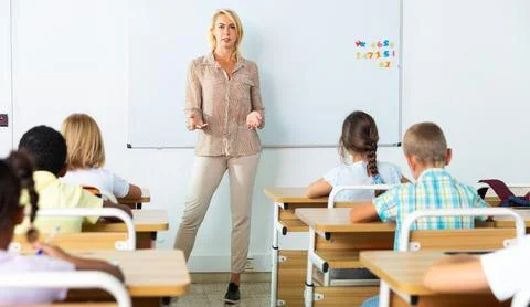 Adult female teacher is giving lecture for primary school students in classroom Stock Photos