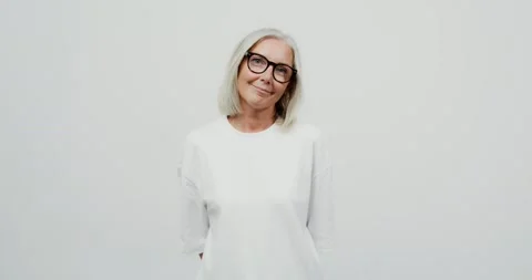 Adult gray-haired woman with glasses playfully smiles looking into the camera Stock Footage