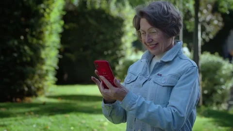 An adult gray haired woman using smartphone in city park. Elderly lady wear Stock Footage 257471353