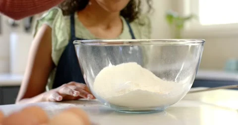 Adult hand entering frame, cracking egg into flour bowl while daughter watching Stock Footage 336058729