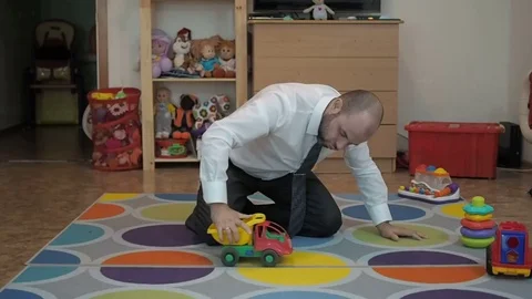 Adult male businessman playing toy cars sitting on the floor in the nursery