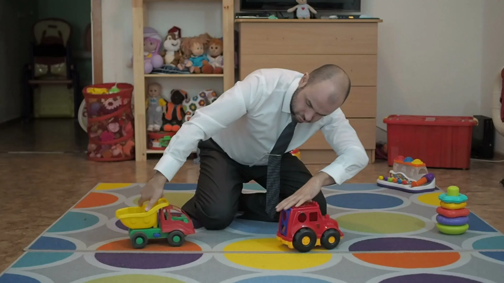 Adult male businessman playing toy cars sitting on the floor in the nursery