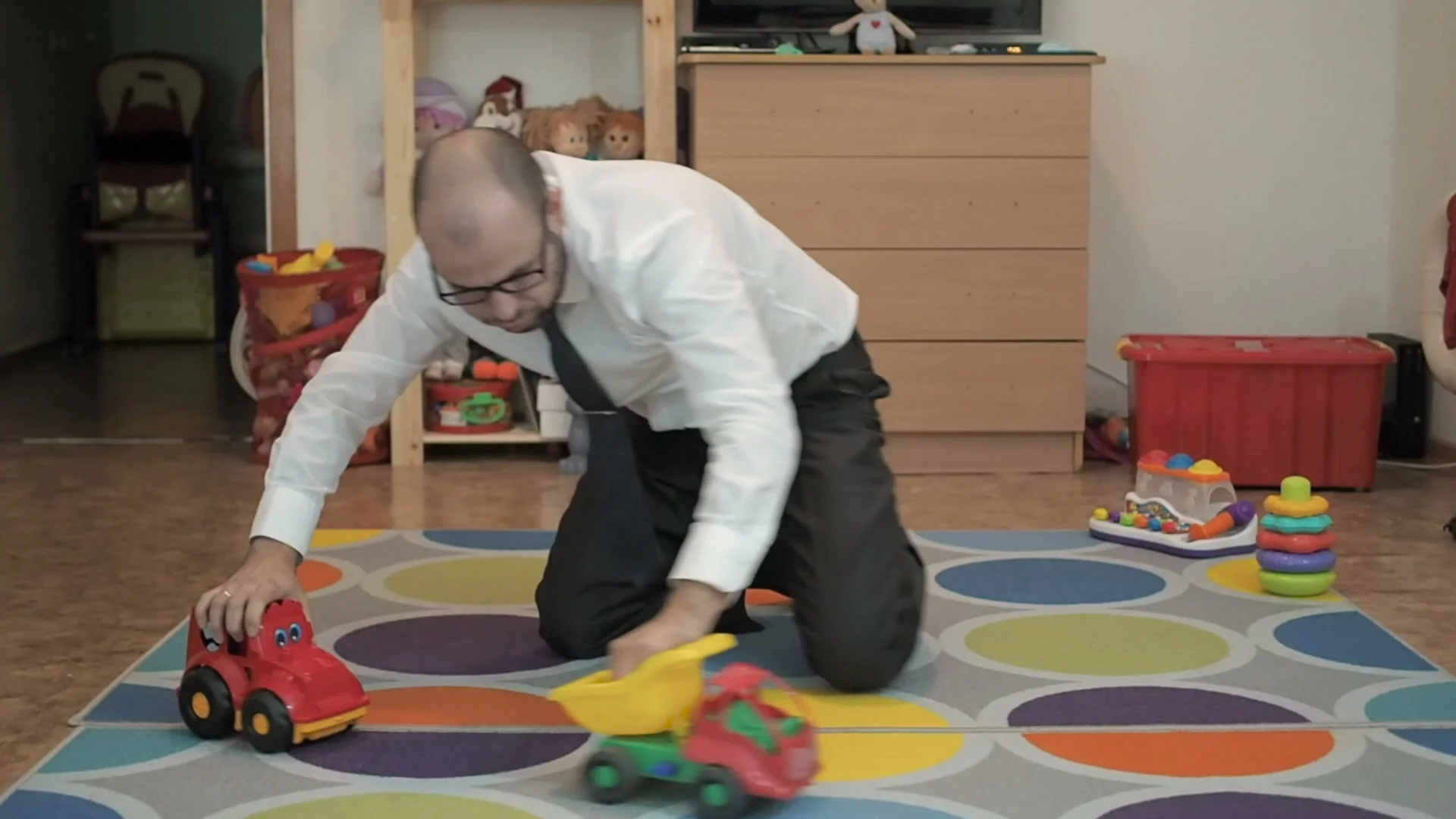 Adult male businessman playing toy cars sitting on the floor in the nursery