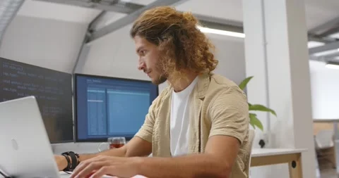 Adult male coder typing seeing code on left monitor pointing and tuning laptop Stock Footage 341061793