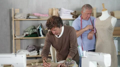 Adult man drawing pattern on paper male assistant sews on mannequin Stock Footage 342128359