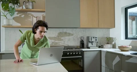 Adult man entering kitchen, using laptop on island, typing data to update Stock Footage 334924054