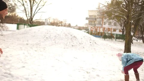 Adult man in a gray down jacket plays snowballs with a teenager girl in a blue Stock Footage 101695918