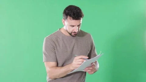 Adult man making notes on paper documents in front of green screen Stock Footage 345575847