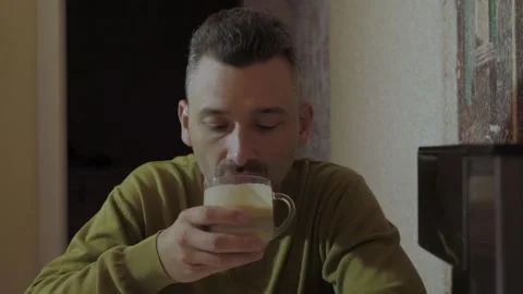 Adult man seated at dining table slowly sipping cappuccino Stock Footage 341832937