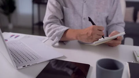 Adult man writing notes in notebook beside laptop during hybrid work sessio.. Stock Footage 345156616