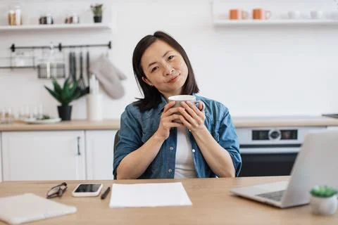 Adult posing with drink while working on laptop in kitchen Stock Photos