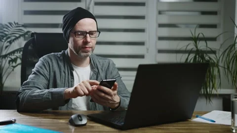 Adult software developer in the workplace. A man uses a smartphone to Stock Footage 182283301