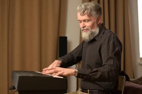 Adult solid gray-haired man with a stylish beard plays the electronic piano Stock Photos