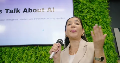 Adult speaker holding mic, explaining, gesturing, pointing to AI slide on stage Stock Footage 338009036