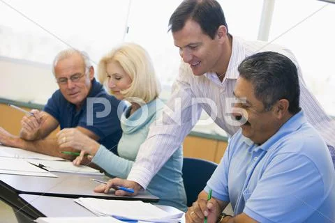 Adult students in class with teacher helping (selective focus) Stock Photos