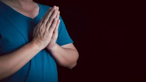 An adult whose hand is prayed on the dark background.Respect for belief in .. Stock Photos