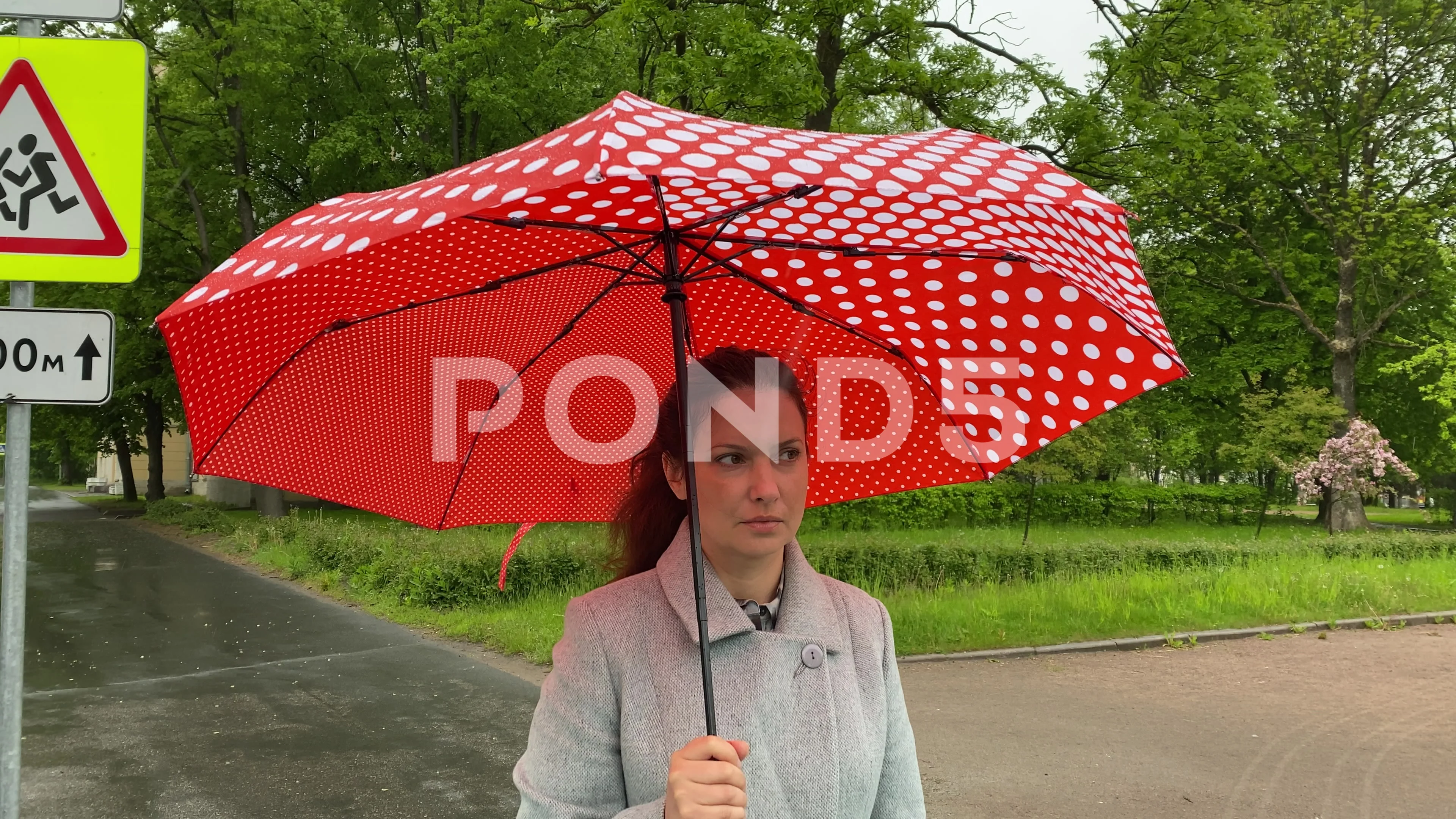 Adult woman in coat hiding under an umbrella in the rain on sidewalk.