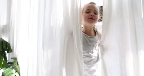 Adult's hand pulls curtain to find child. Girl hiding behind curtain Stock Footage 248043649