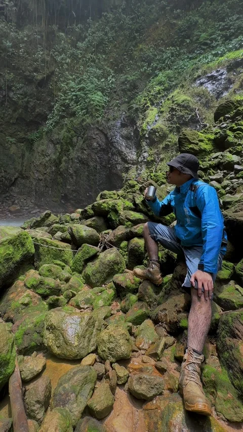 Adventurer Drinking, Observing in Rainforest, Pan to Tall Waterfall, Vertical Sh Stock Footage 321104247