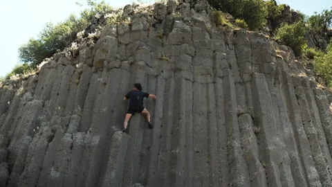 Adventurous Climber Scaling Steep Basalt Rock Formation on a Sunny Day in Nature Stock Footage 278731617