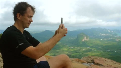 Adventurous man captures panoramic views using smartphone at mountain Stock Footage 260637306