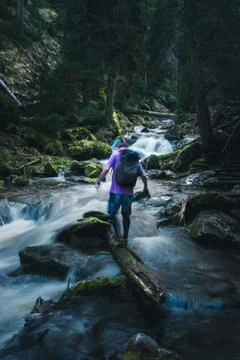 An adventurous man carrying a backpack skillfully crosses a river on a log Stock Photos