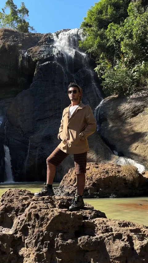 Adventurous Man Posing by Jungle Waterfall on Sunny Day, Vertical Stock Footage 325646673