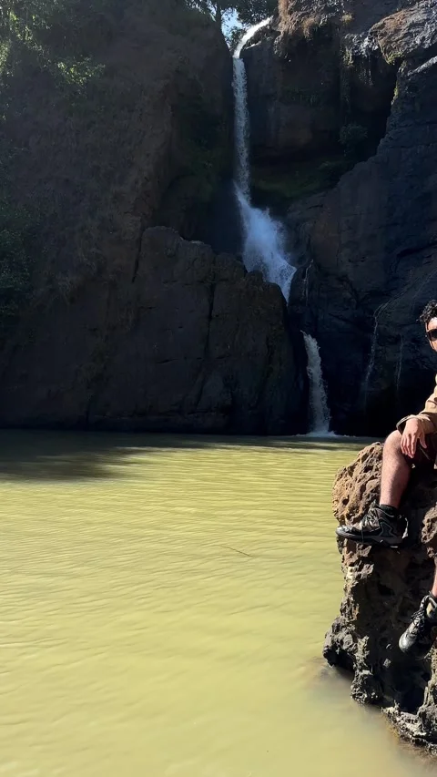 Adventurous Man Posing by Waterfall, Tropical River Scene, Vertical Pan Stock Footage 325645240