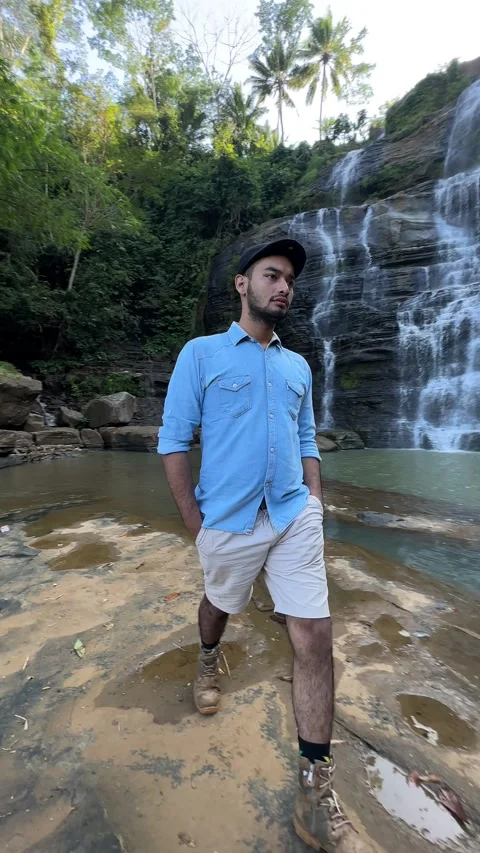 Adventurous Man Walks Past Cascading Waterfall in Tropical Forest, Vertical 스톡 동영상 324772592