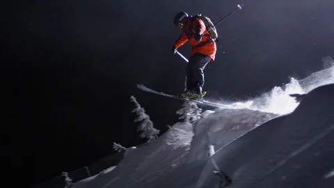 Adventurous skier jumping down the snowy mountain slope at night Stock Footage 116738473