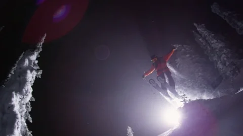 Adventurous skier jumping down the snowy mountain slope at night Stock Footage 116738556