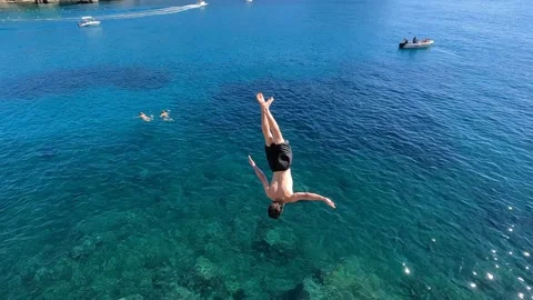 Adventurous young man jumping off a cliff does a backflip in Greece Stock Footage 257545280