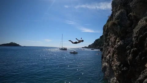 Adventurous young man jumping off a cliff does a backflip in Greece Stock Footage 257545390