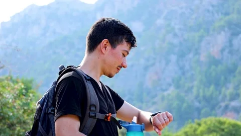 Adventurous young man looking at watch surrounded by mountains Stock Footage 293569108