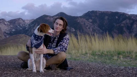 Adventurous Young Man Sits With His Dog And Watches The Sunset, He Pets Her Stock Footage 70041031