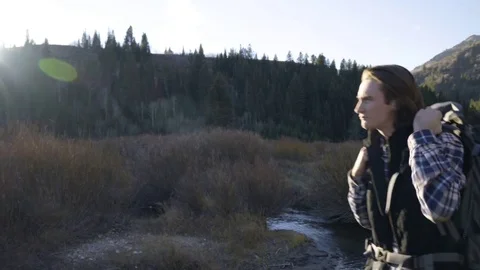 Adventurous Young Man Takes Off His Pack, Sits Down By Creek, Searches Inside Stock Footage 70040686