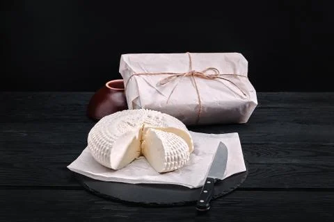 Adyghe cheese cut off a triangular piece. Nearby are three cheese heads packed Stock Photos