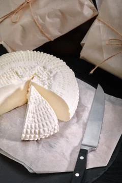 Adyghe cheese cut off a triangular piece. Nearby are three cheese heads packed Stock Photos
