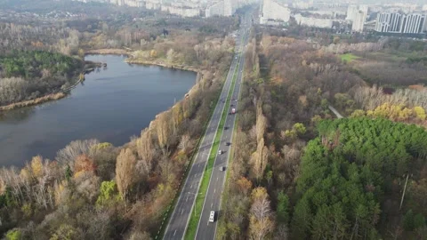 Aerial 4K boulevard between lake and forest with city skyline ahead 스톡 동영상 323162553