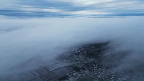 Aerial 4K forward flight along fog bank revealing winter town Video stock 323162234