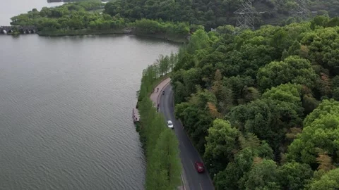 Aerial 4K view of the road between forest green trees and lake, Hangzhou, China Stock Footage 240626184