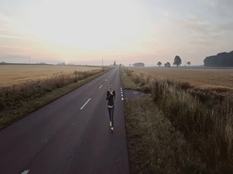 AERIAL 4K: Woman Running on a Countryside Road at Morning, at Sunrise. Stock Footage